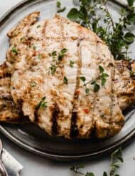 Italian Grilled Chicken surrounded by fresh herbs, on a gray plate.