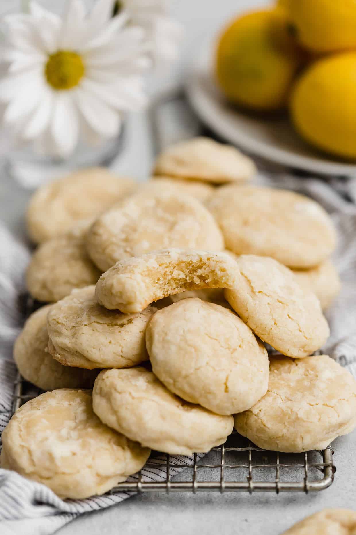 A lemon cookie with a bite taken out of it, stacked on a pile of other baked lemon cookies.