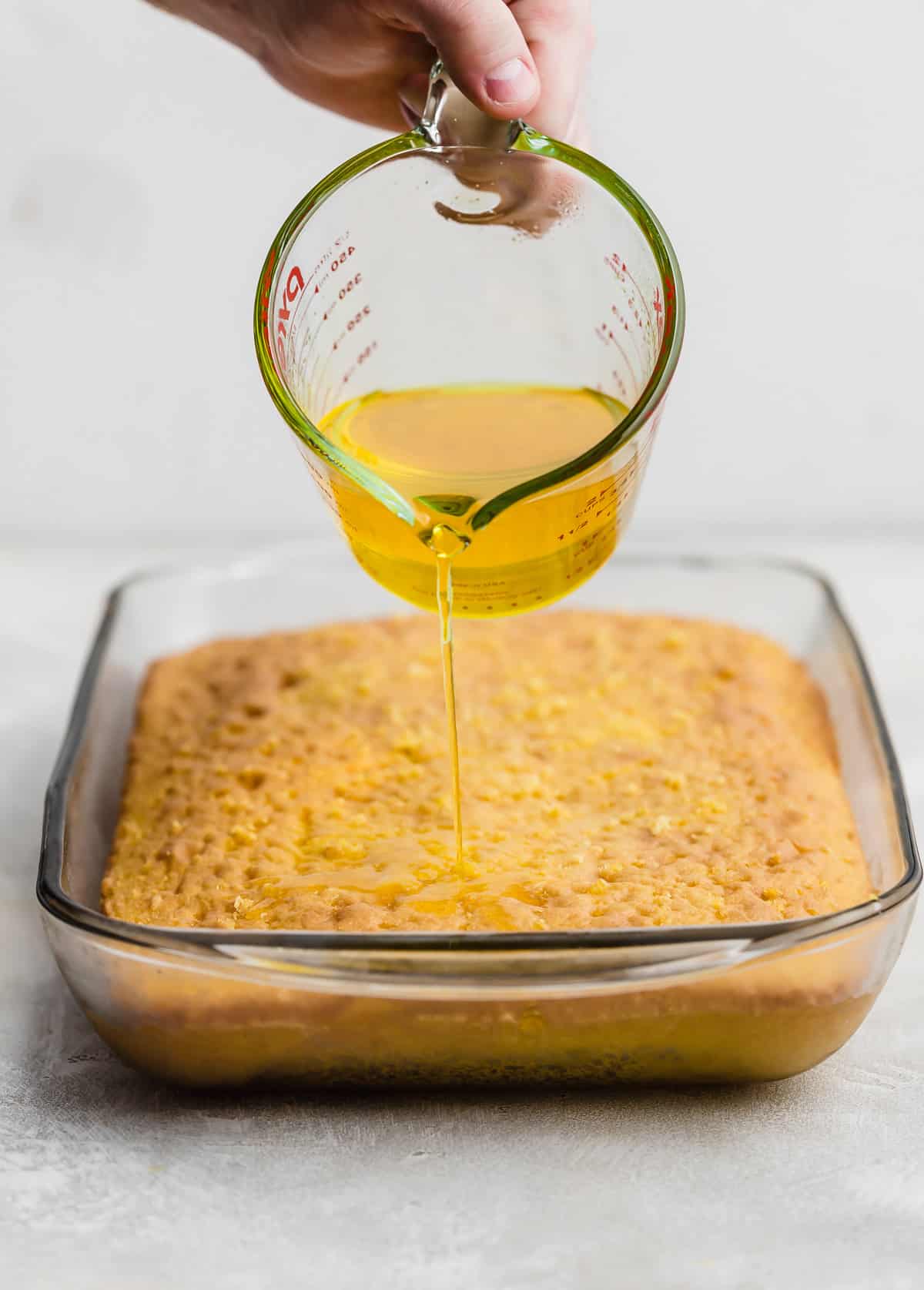Lemon jello liquid mixture being poured overtop a baked lemon cake.