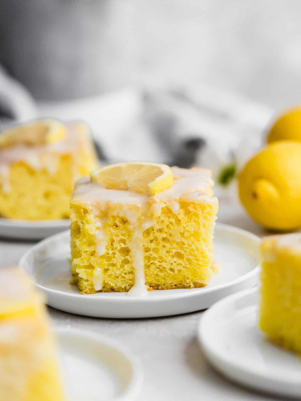 A slice of Lemon Jello Cake topped with a white glaze and a fresh lemon wedge.