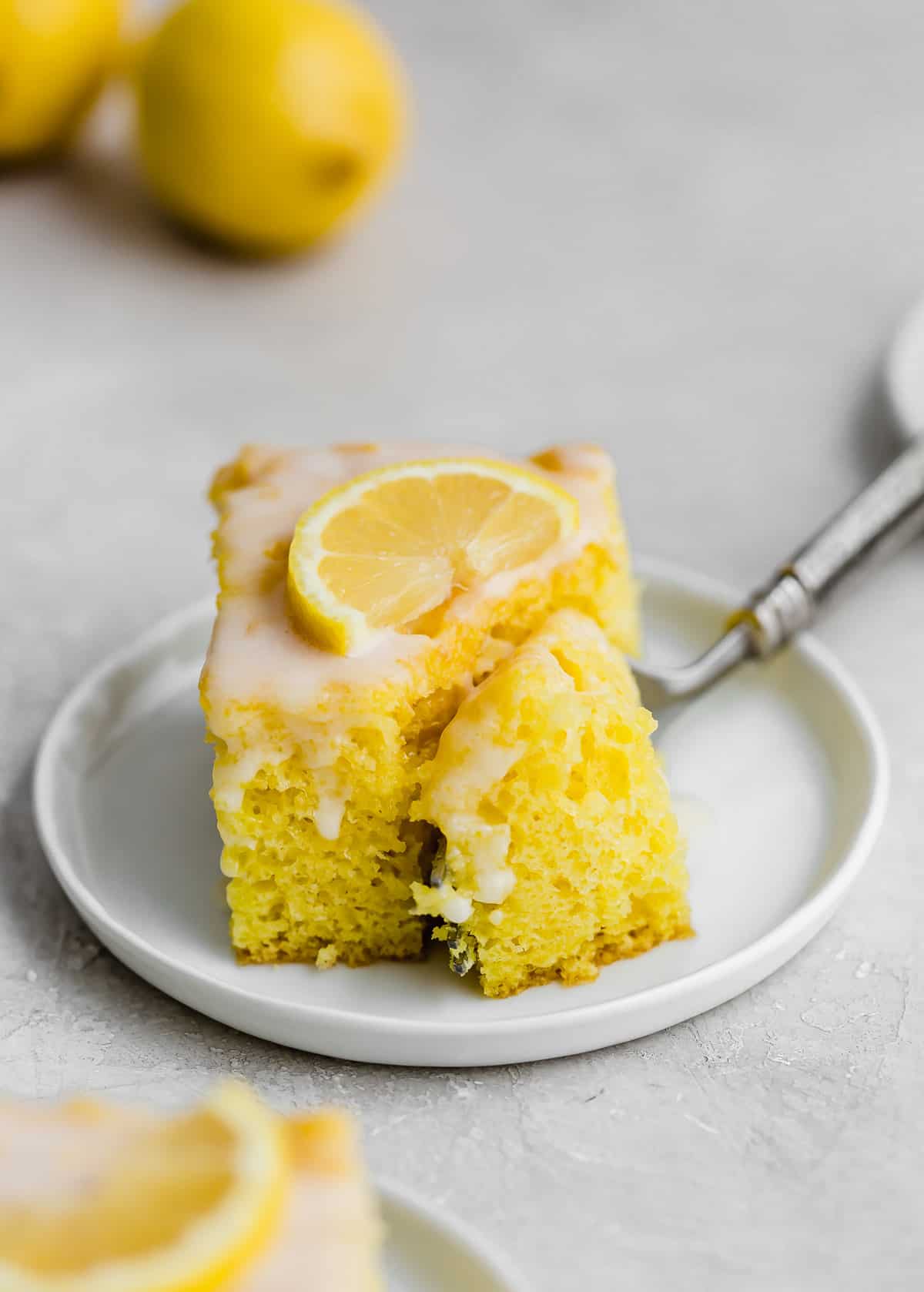 A fork cutting into a square of lemon jello cake on a white plate.