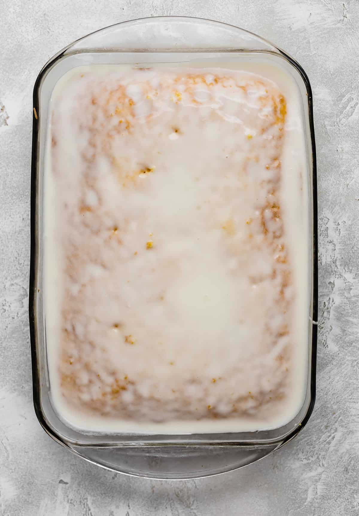 A white glaze topped lemon cake in a rectangular glass dish.