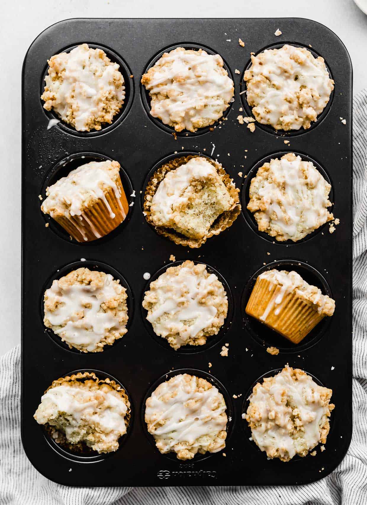 A muffin tin with baked Lemon Poppy Seed Muffins with a crumb topping and glaze.