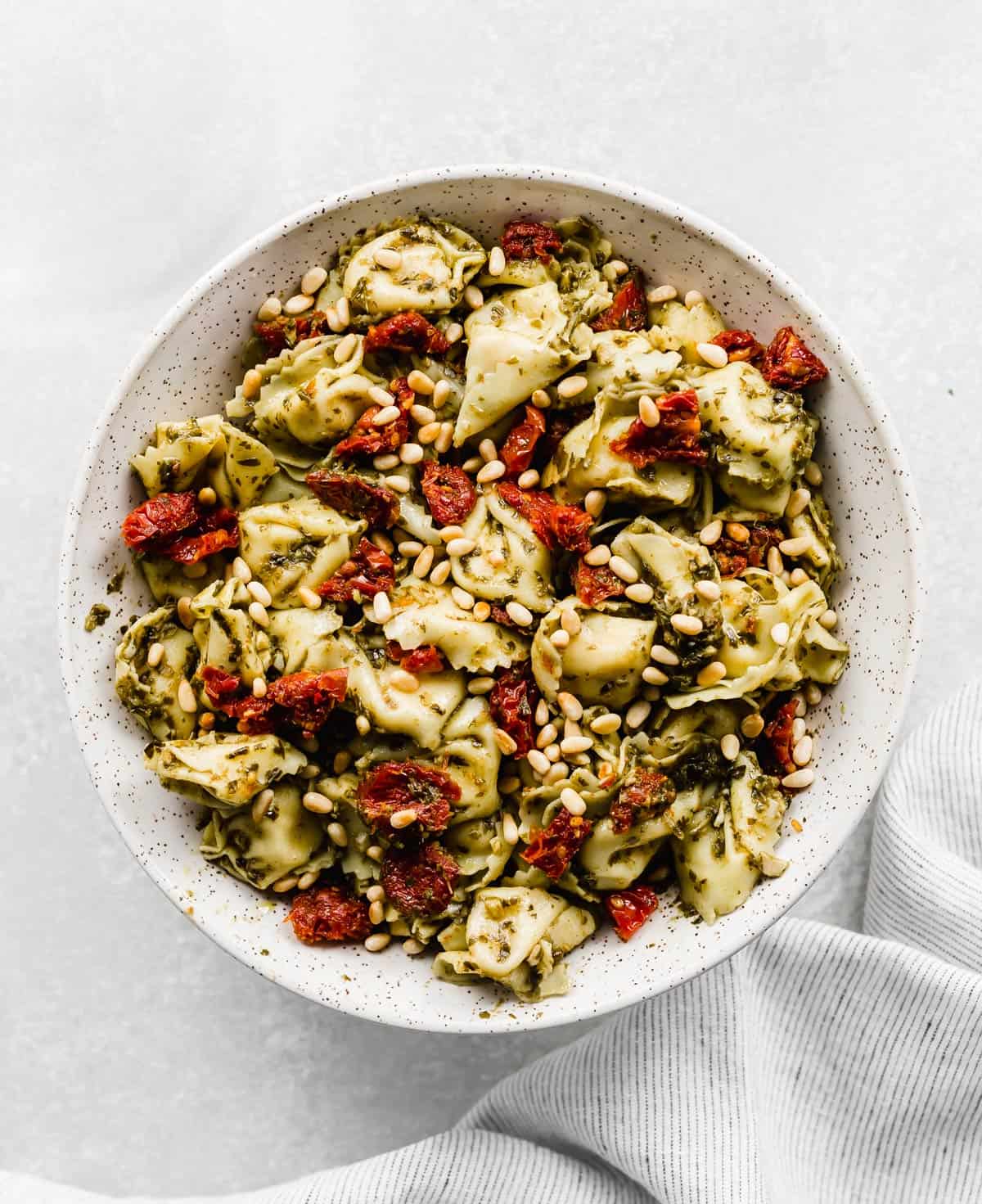 A large bowl with Pesto Tortellini Pasta Salad with pine nuts and sun-dried tomatoes.