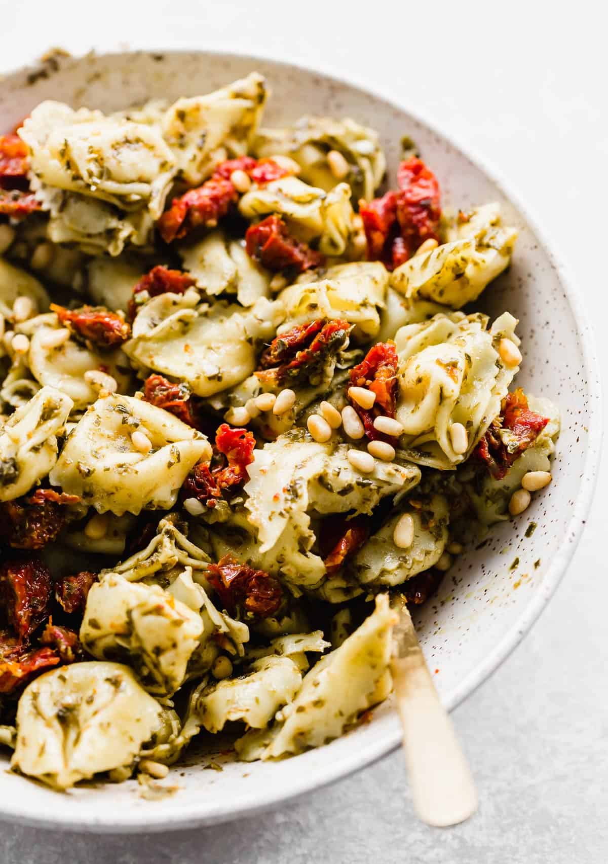 A close up photo of Pesto Tortellini Pasta Salad with sun-dried tomatoes and pine nuts in the salad. 