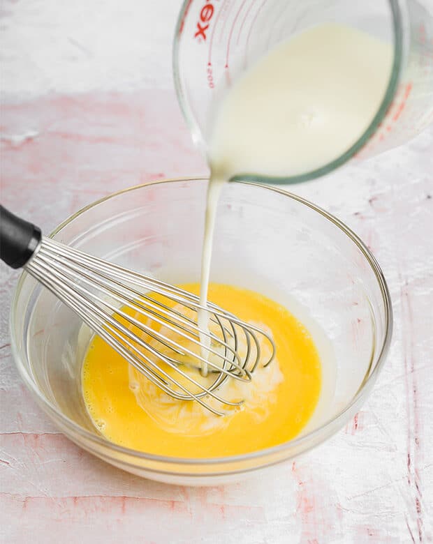 Warm cream being poured into a bowl of egg yolks.