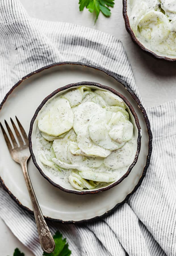 Overhead photo of a Creamy Cucumber Salad in a small bowl sitting on a dinner plate. 