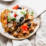 An easy Mexican Lasagna recipe on a white plate, the lasagna is topped with sour cream, olives, tomatoes, and lettuce.