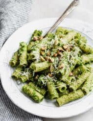 A white plate with kale pesto pasta on it, topped with chopped pistachios.