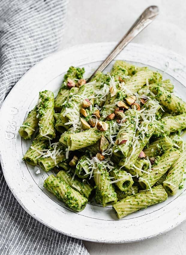A white plate with kale pesto pasta on it, topped with chopped pistachios. 