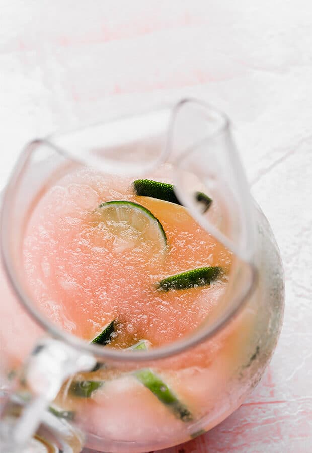 Overhead photo of lime slices in a glass pitcher with a pink limeade drink.