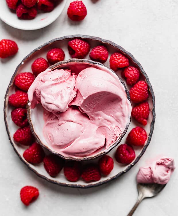Overhead photo of raspberry ice cream in a bowl against a white background.