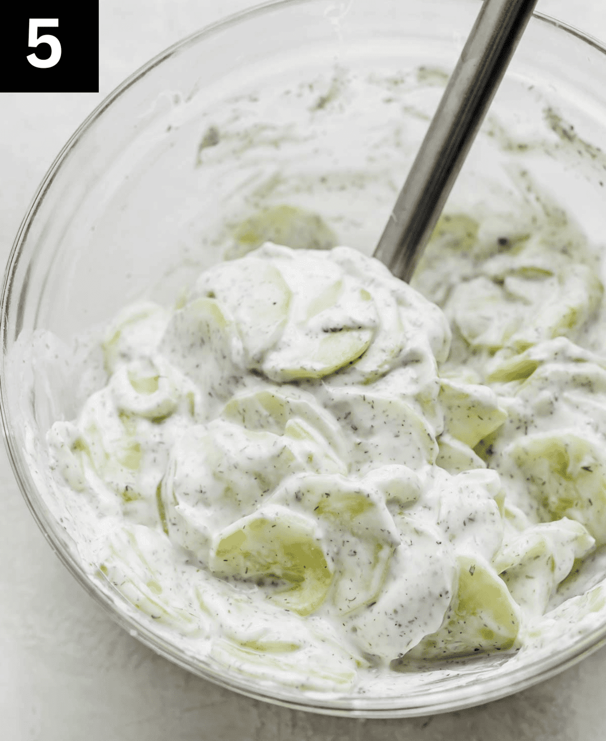 Sliced cucumbers in a white creamy yogurt seasoned dressing.