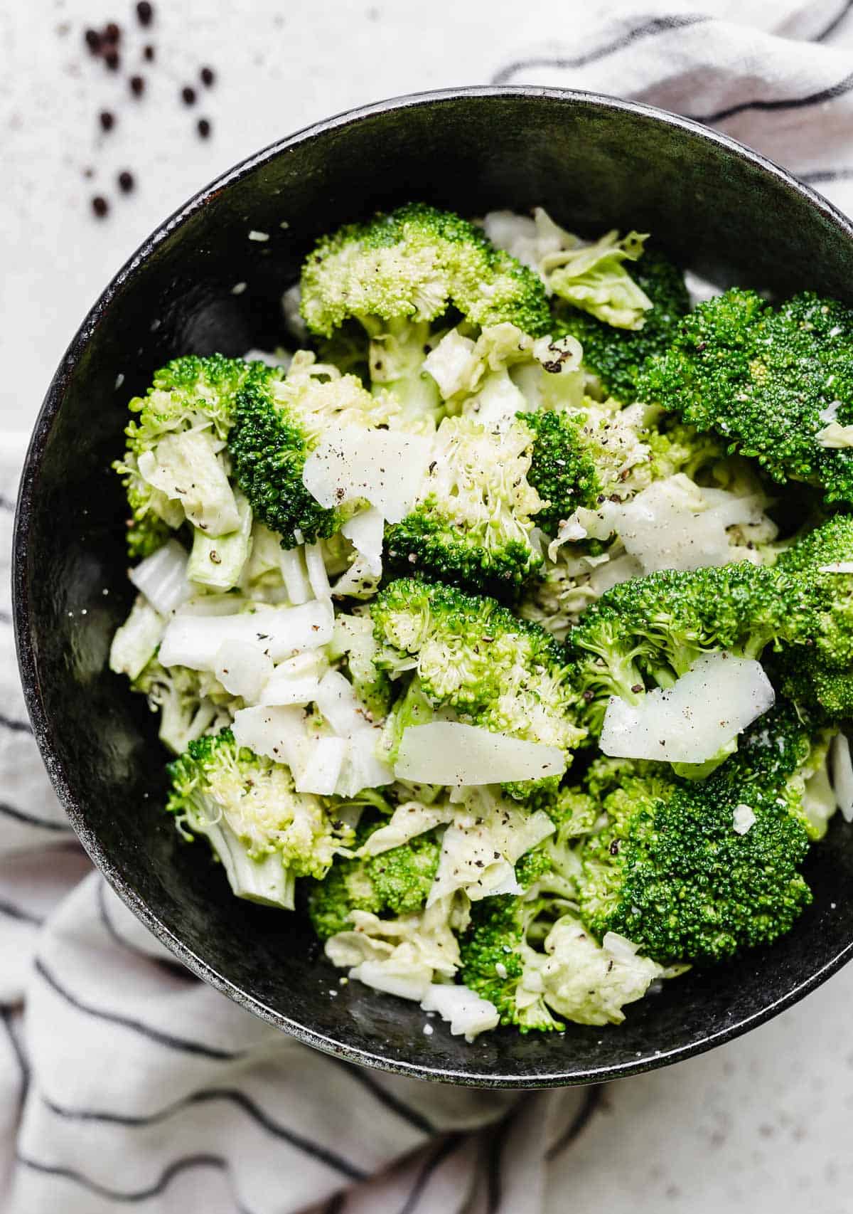 A Broccoli Caesar Salad cut into florets in a black bowl with shaved parmesan.