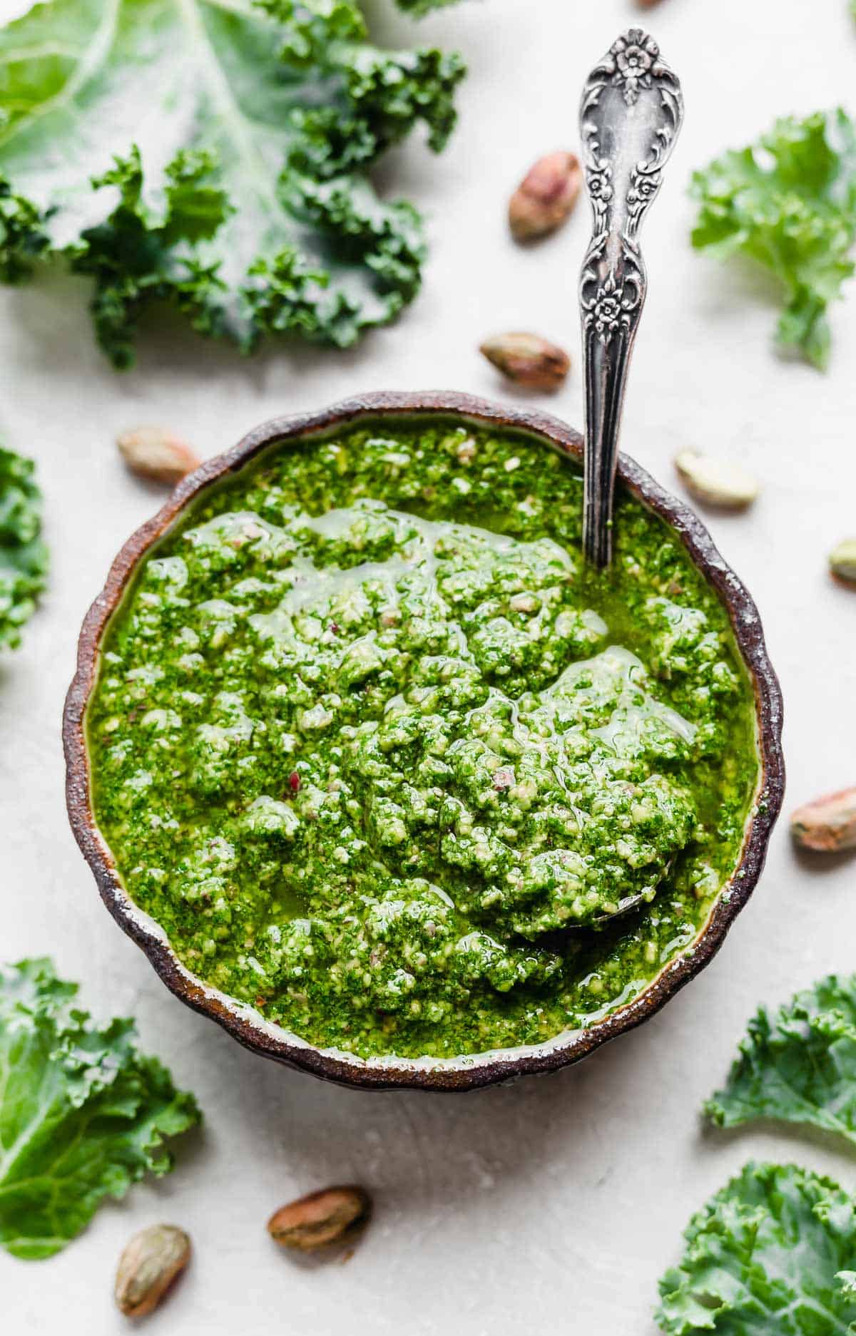 Overhead photo of Kale Pesto in a black bowl surrounded by pistachios.