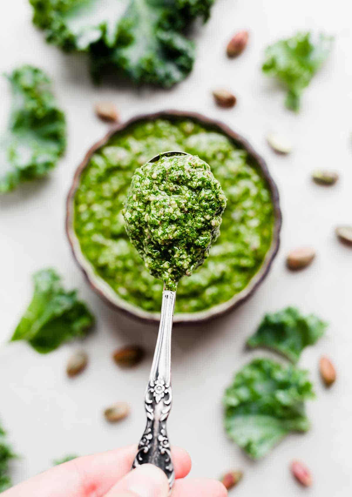 A spoon holding up Kale Pesto above a bowl of Kale Pesto.