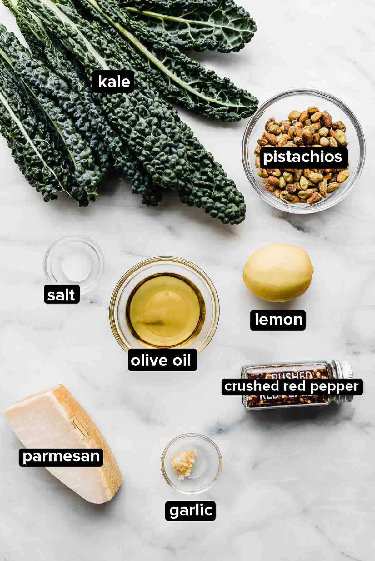 Kale Pesto ingredients on white background: kale, olive oil, pistachios, garlic, parmesan.