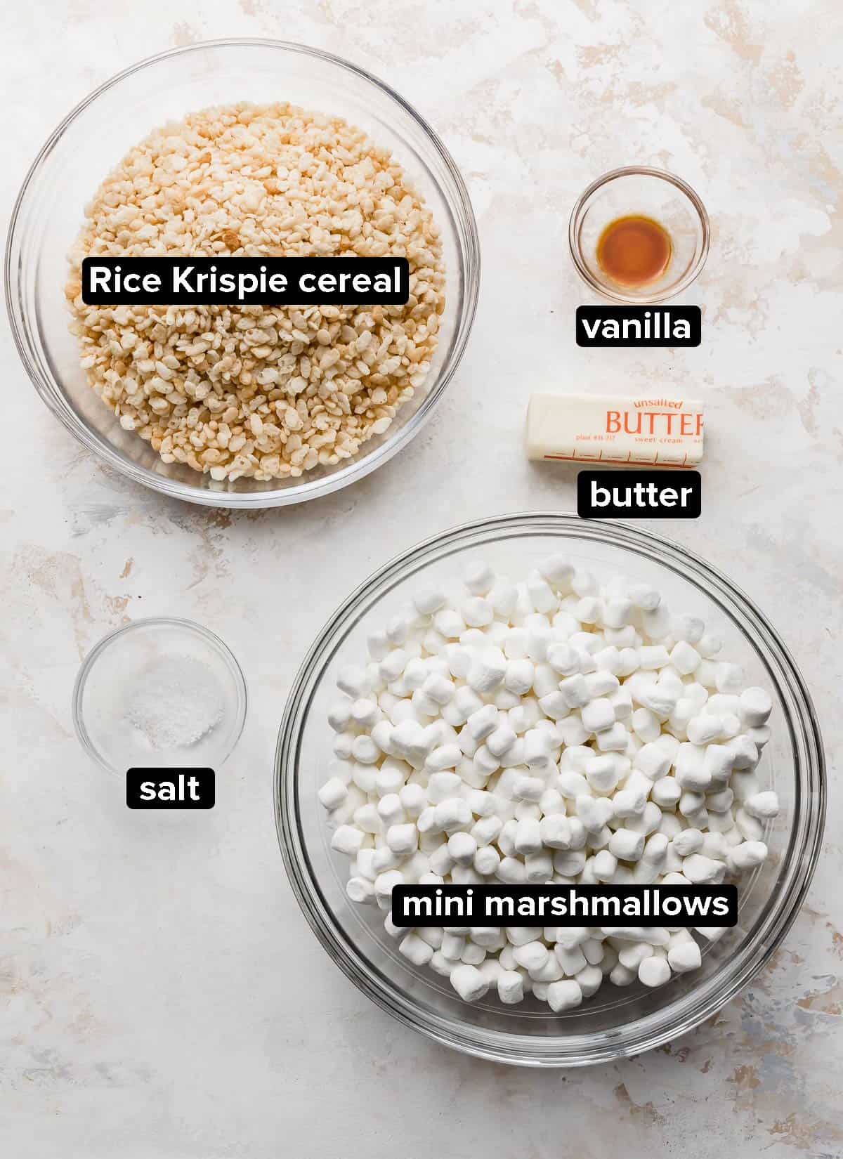 Rice Krispies Treats ingredients in glass bowls on a white textured background.