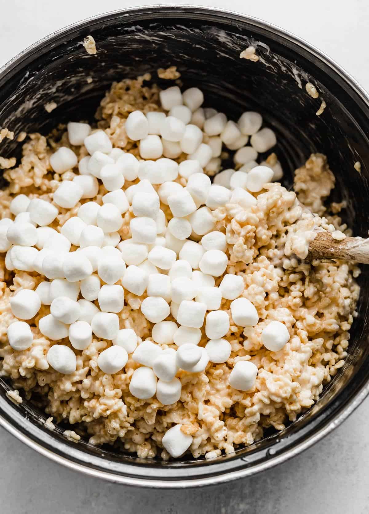 Mini marshmallows poured on top of a Rice Krispies Treats mixture in a black pot.