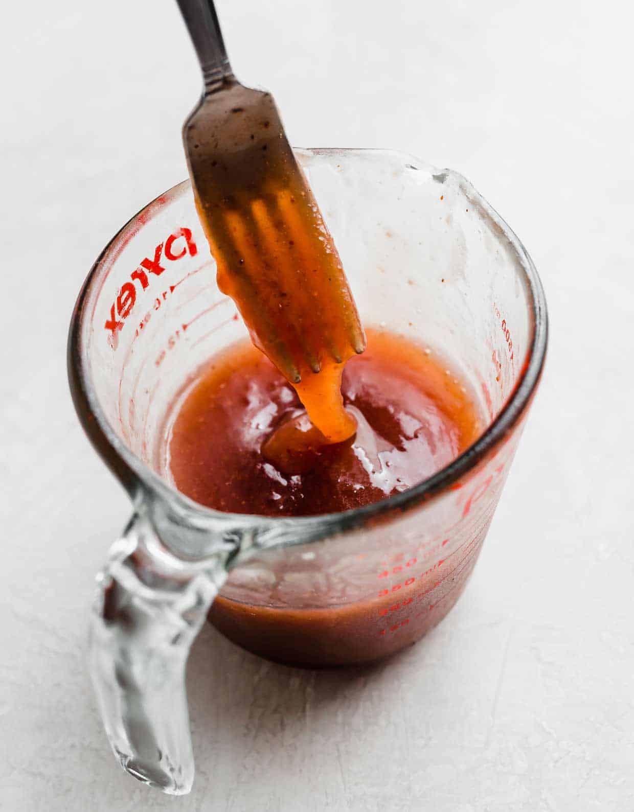 A homemade strawberry vinaigrette dressing in a glass measuring cup on a white background.
