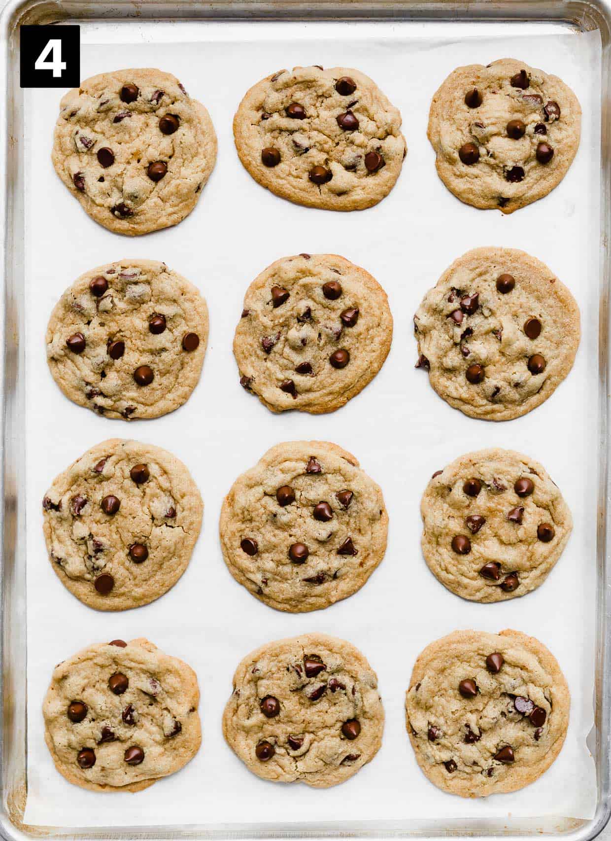 Twelve baked Tahini Chocolate Chip Cookies on a white parchment lined baking sheet.