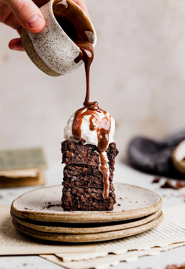 A stack of homemade brownies on a plate topped with a scoop of ice cream and a drizzle of hot fudge.