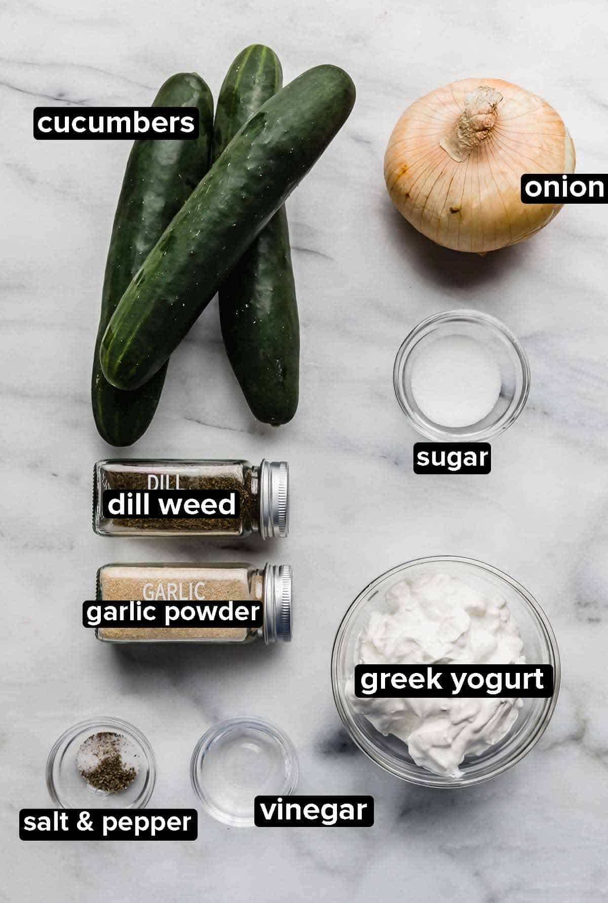 Creamy Cucumber Salad ingredients on a white marble background.