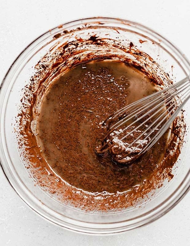 A whisk stirring a chocolate mixture and melted butter in a bowl.