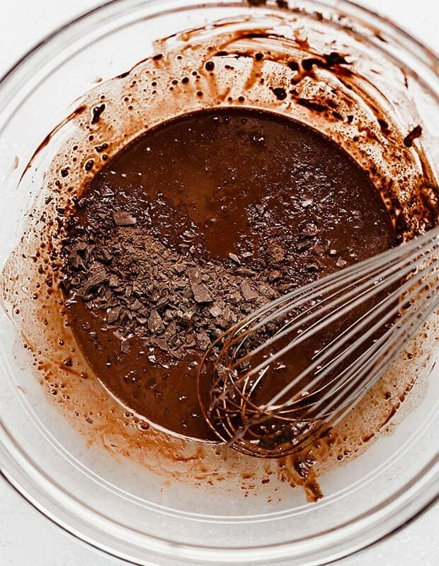 A glass bowl with cocoa, hot water, and chopped chocolate in it.