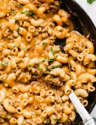 A close up photo of macaroni noodles, ground beef, and a cheesy sauce in a cast iron skillet.