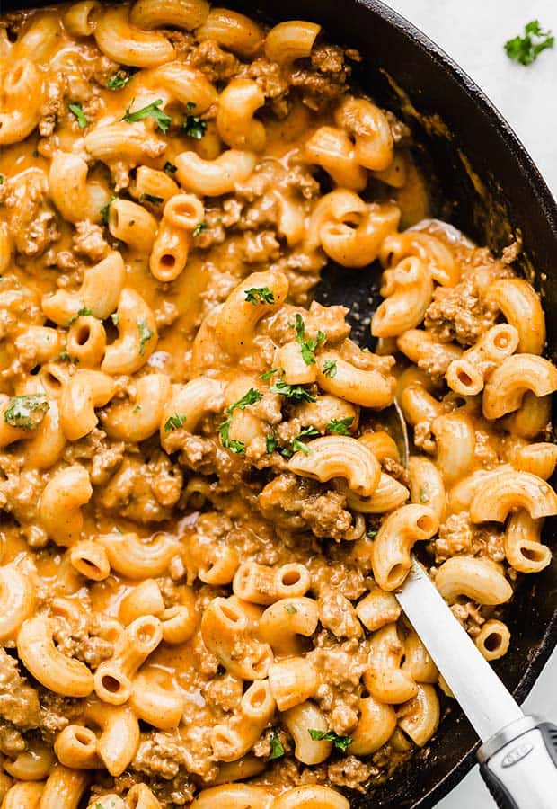 A close up photo of macaroni noodles, ground beef, and a cheesy sauce in a cast iron skillet.