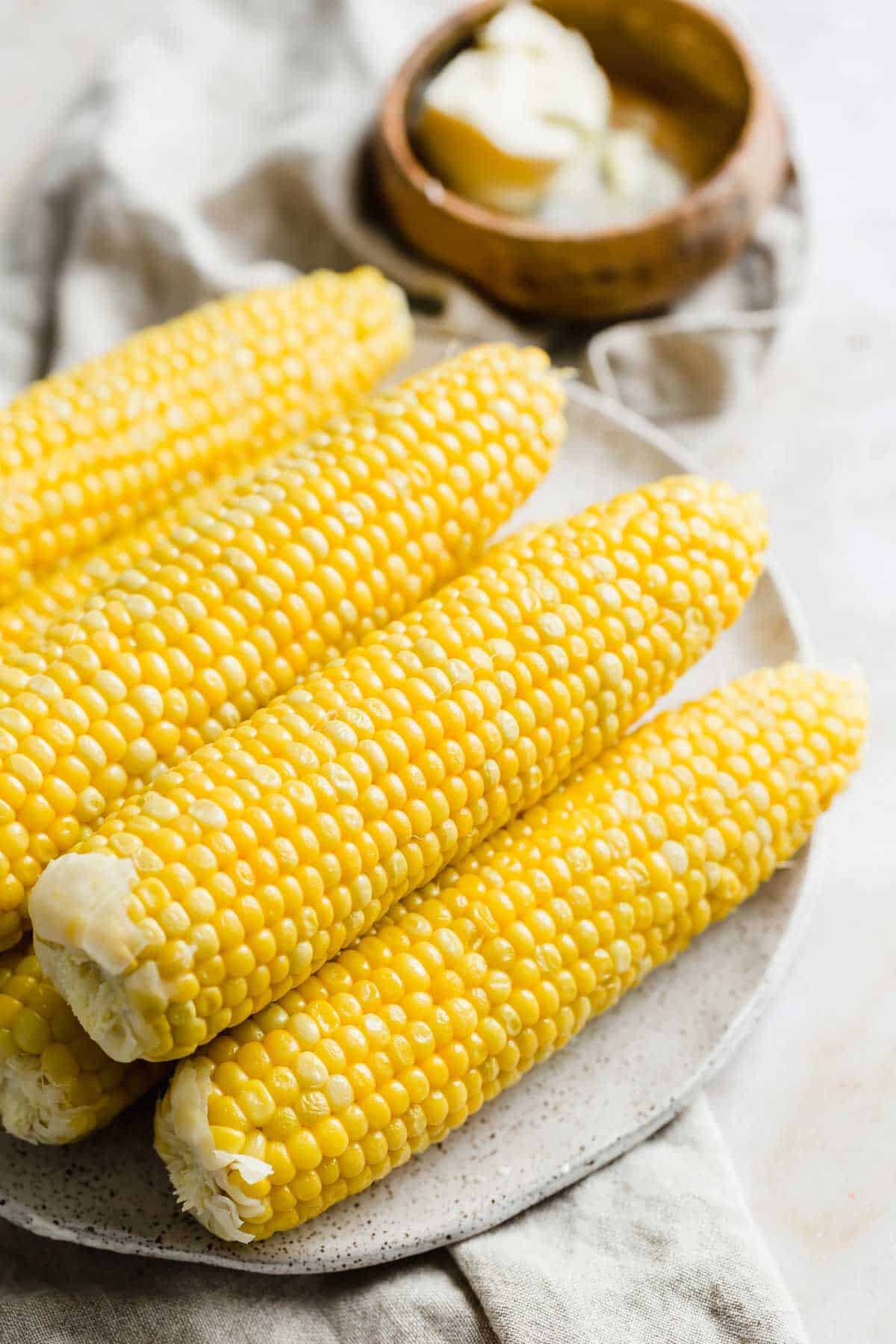 Perfectly boiled corn on a white plate with a bowl of butter in the background.
