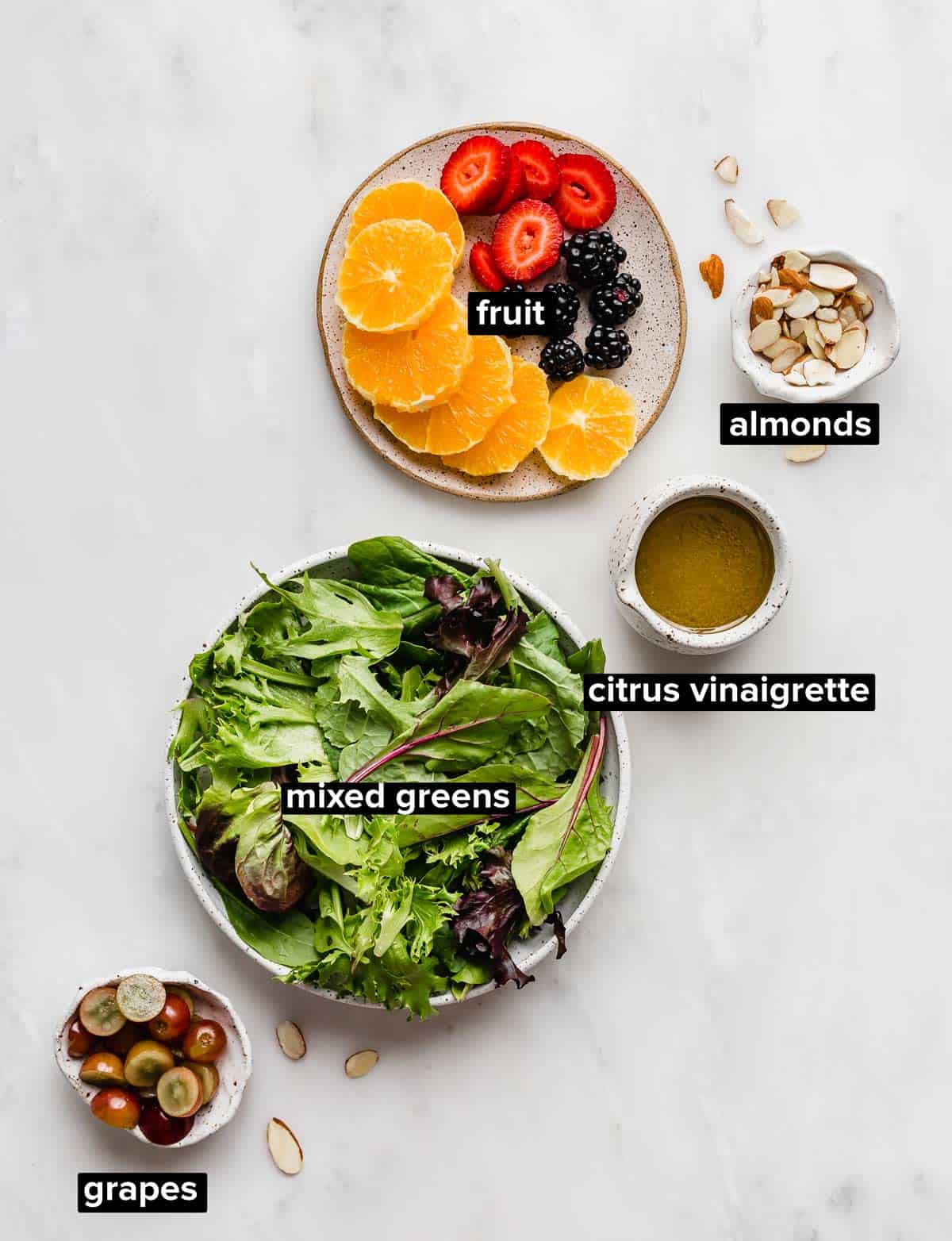 Citrus Summer Salad ingredients on a white background: mixed greens, fruit, citrus vinaigrette, almonds, and grapes.