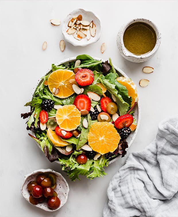 A lettuce salad topped with fresh fruit, sliced almonds, and grapes.