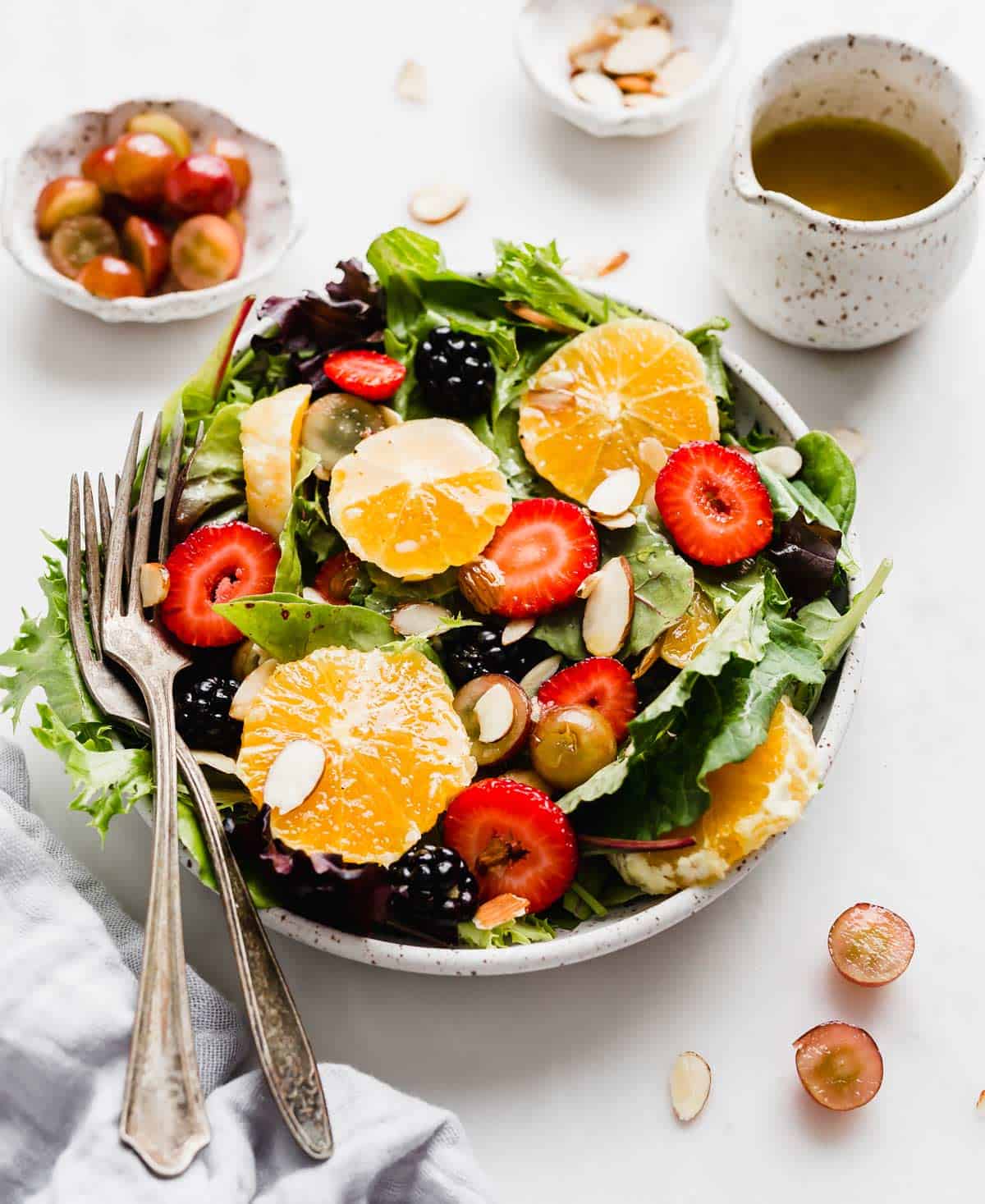 A summer salad topped with oranges, strawberries, blackberries, grapes, and almonds.