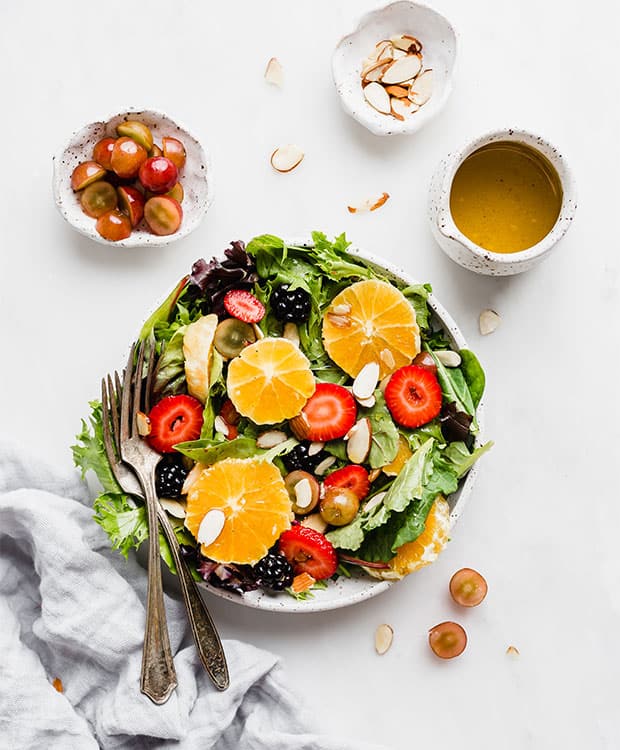 A plate full of salad greens, sliced oranges, almonds, and strawberries.