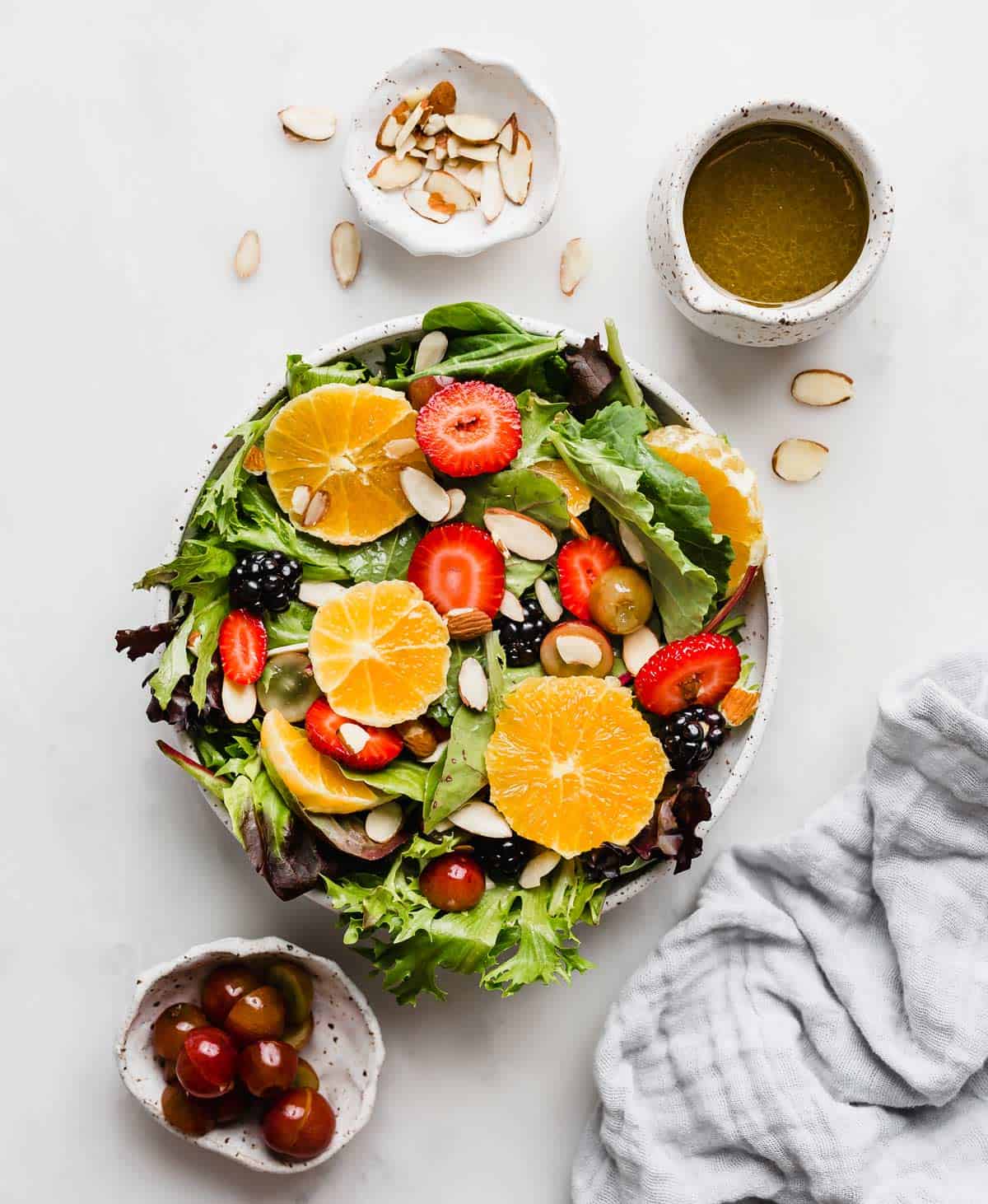 A citrus salad with oranges, strawberries, blackberries, grapes and almonds on a bed of mixed greens.