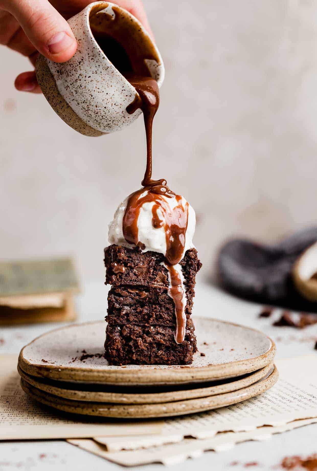 Two Homemade Fudgy Brownies stacked on top of each other, a scoop of vanilla ice cream on top, and hot fudge sauce drizzled over the ice cream.