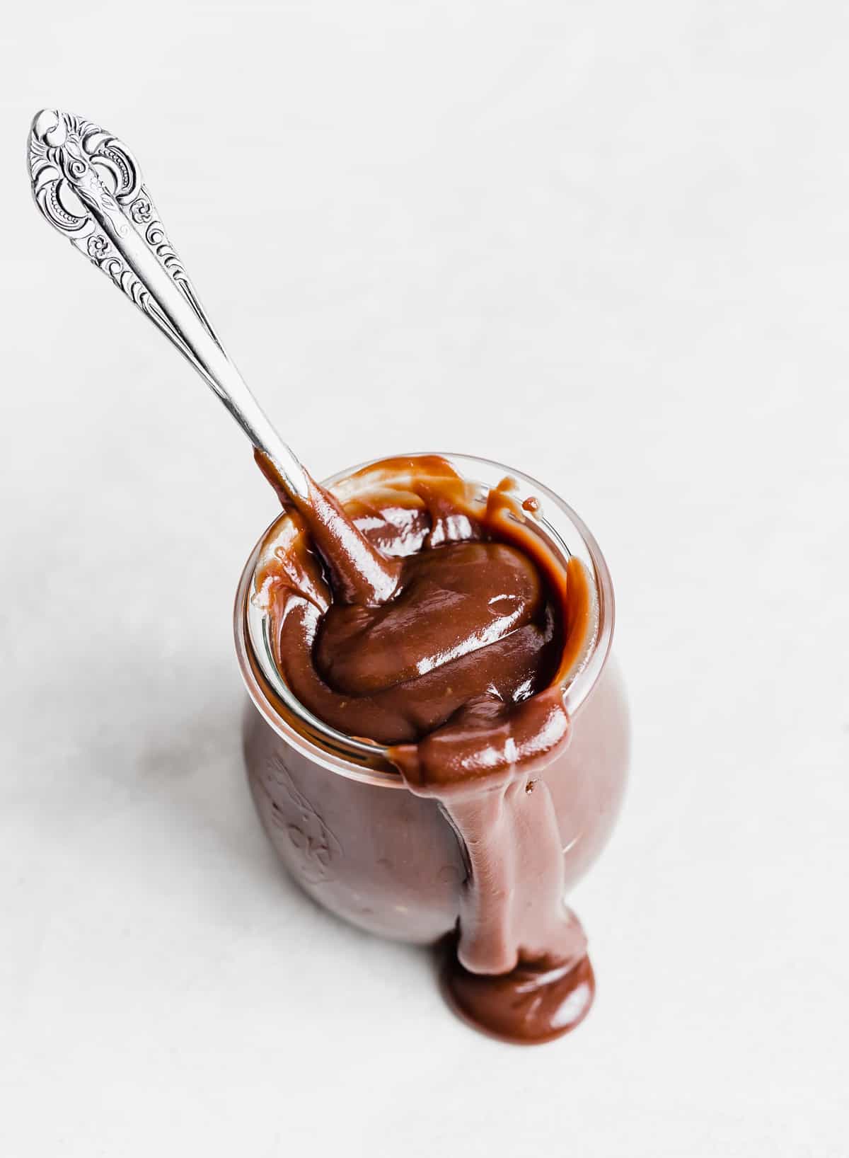 Old fashioned Hot Fudge Sauce in a glass jar on a white background. 
