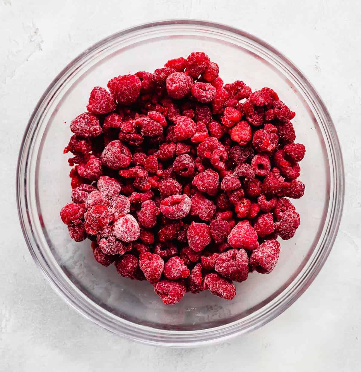 Frozen raspberries in a glass bowl on a white background.