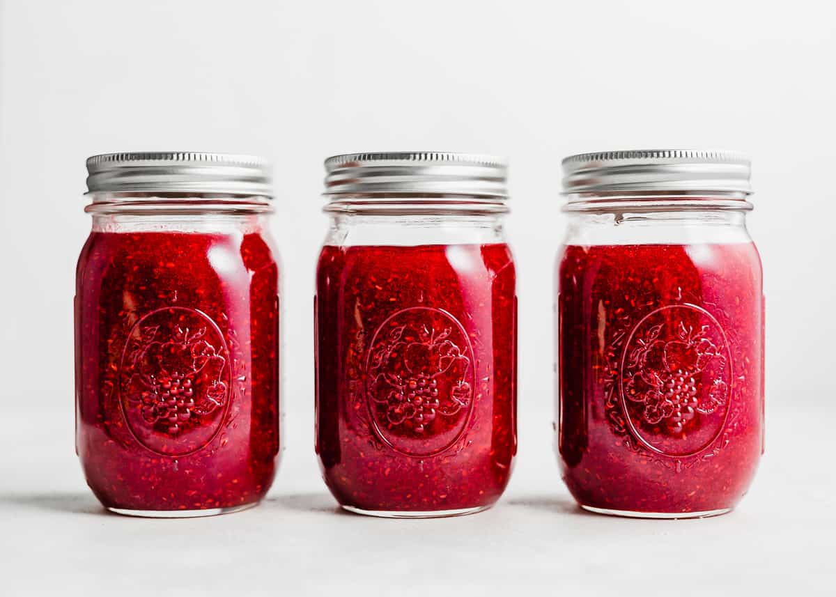 Three Raspberry Freezer Jam jars against a white background.