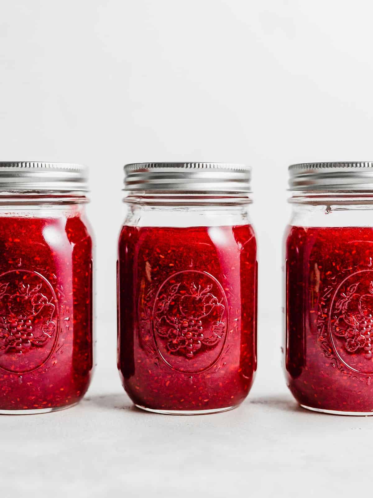 Three jars of Raspberry Freezer Jam on a white background.