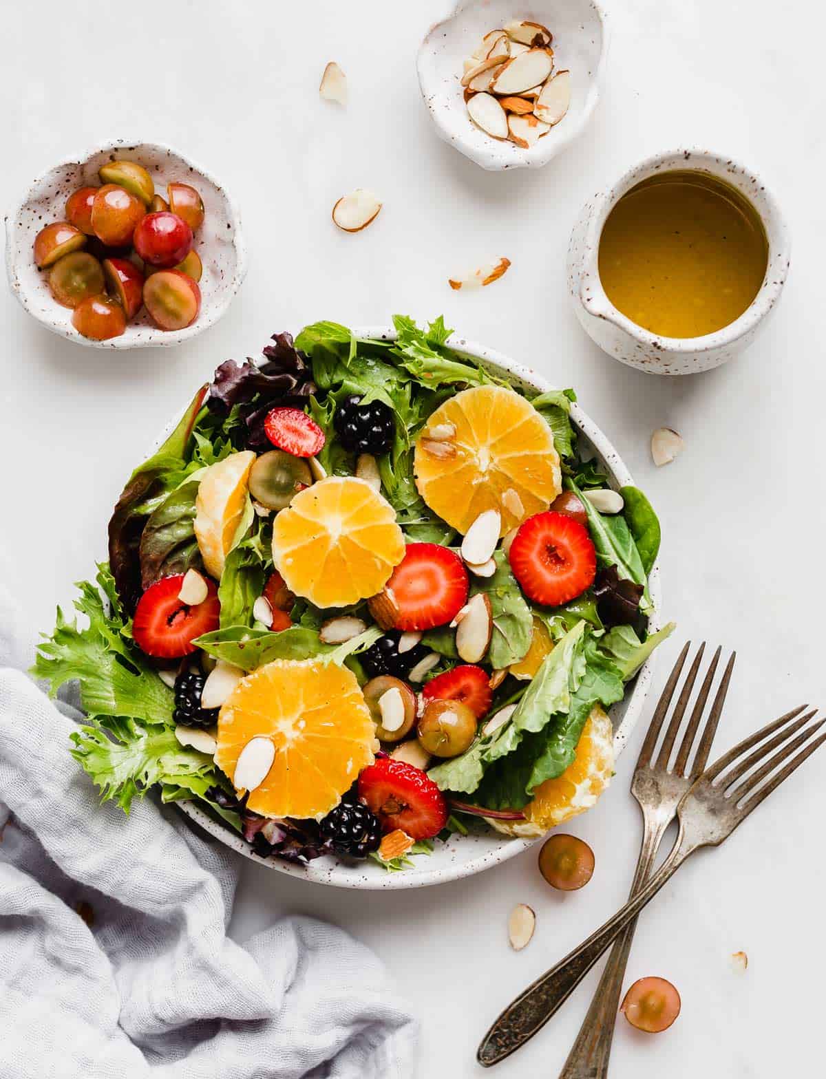 Citrus Salad on a white plate; mixed greens, strawberries, oranges, blackberries, grapes, and a citrus vinaigrette to the side.