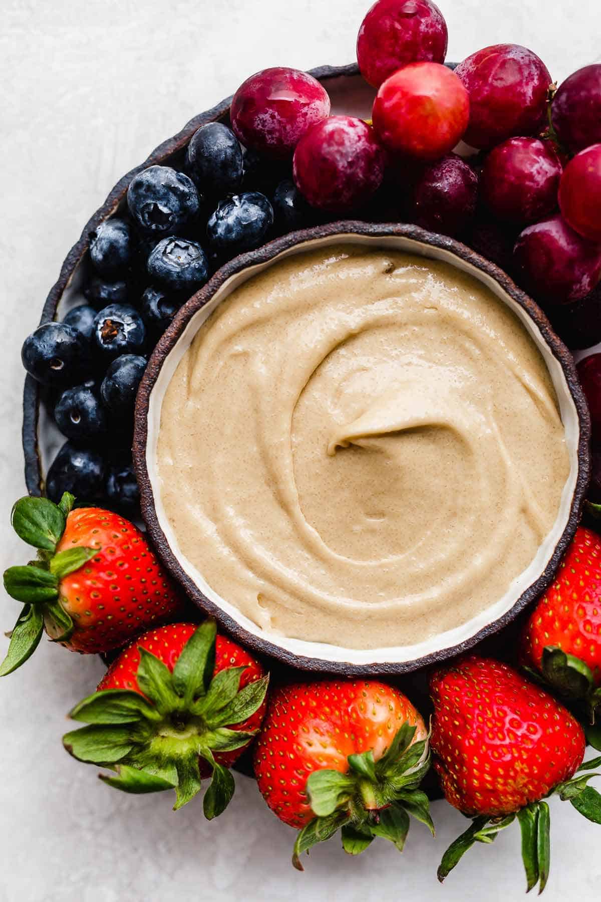 Cream Cheese Fruit Dip in a black bowl with strawberries, grapes, and blueberries around the bowl.