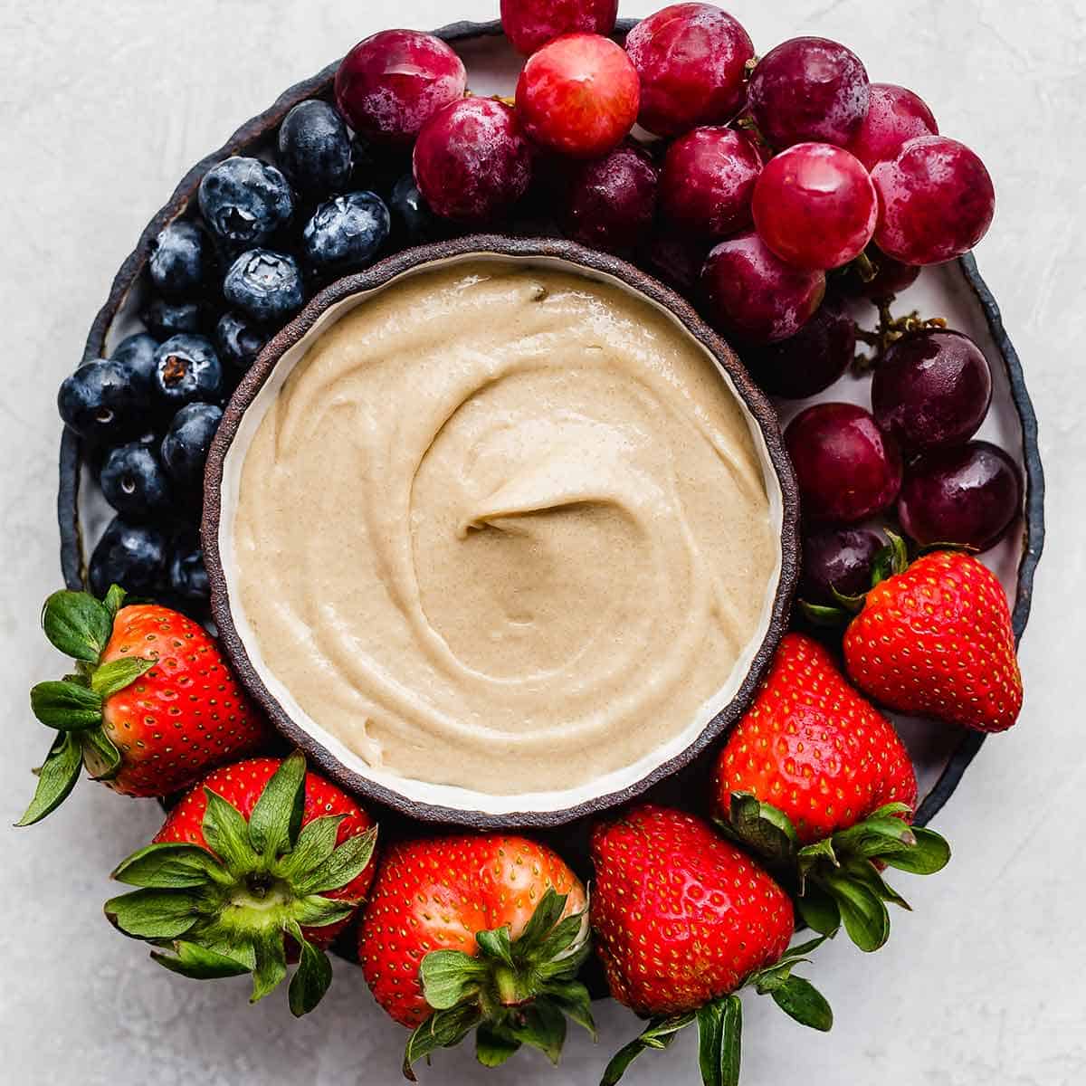 Cream Cheese Fruit Dip surrounded by grapes, strawberries, and blueberries.