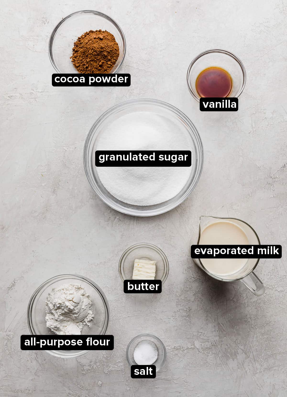 Hot Fudge Sauce ingredients in glass bowls on a white marble background.