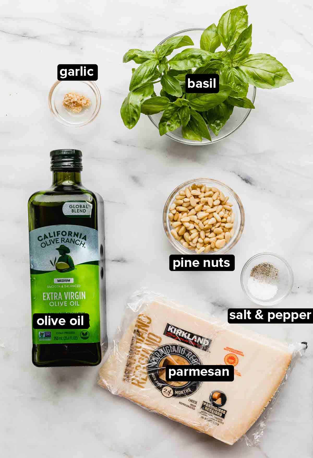 Basil Pesto ingredients on a white background: pine nuts, olive oil, basil, garlic, salt and pepper, and parmesan. 