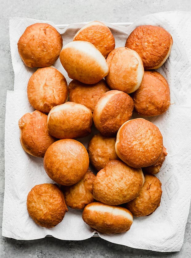 A pile of golden brown doughnuts on a white background.