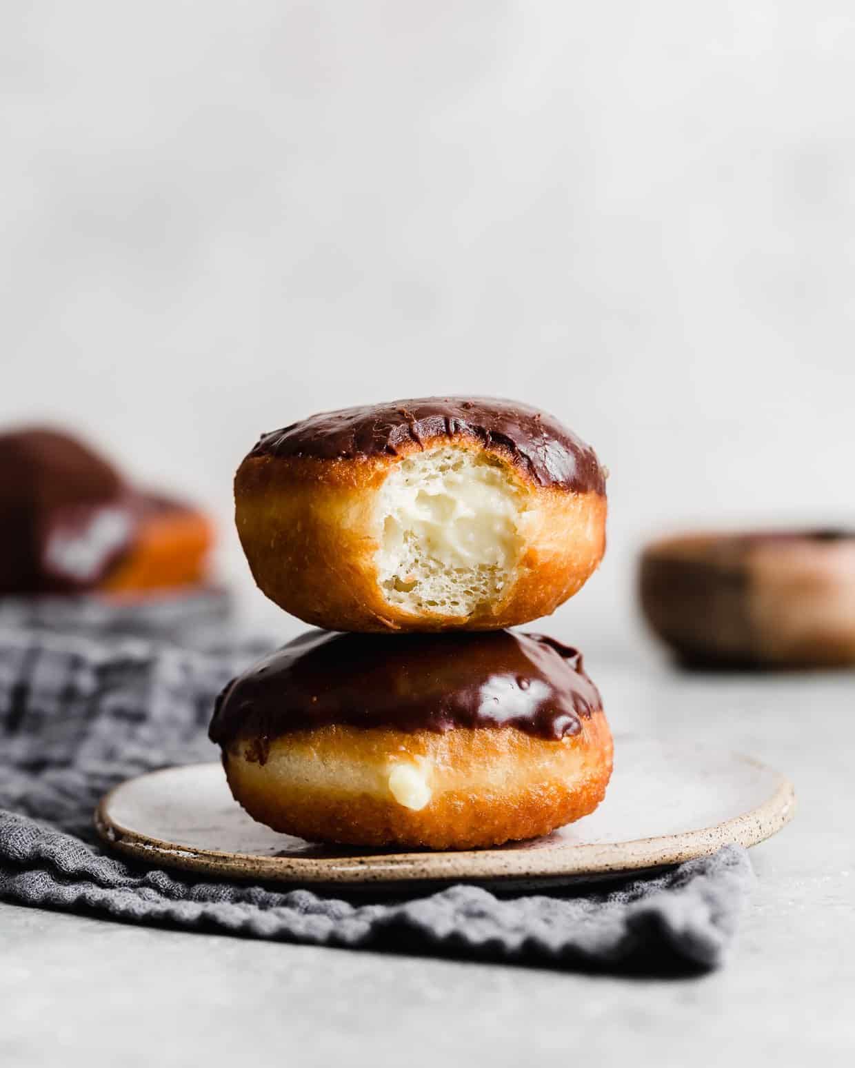 Two Boston Cream Donuts stacked on top of each other, with the top donut having a bite taken out of it. 