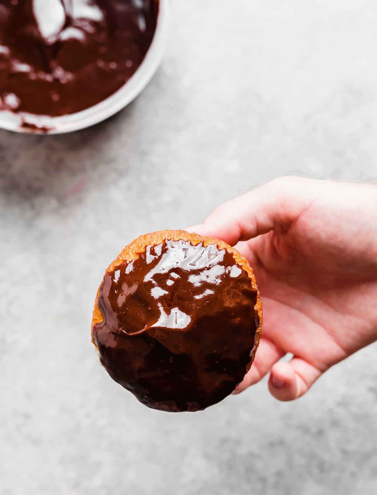 A hand holding a chocolate dipped Boston Cream Donut.